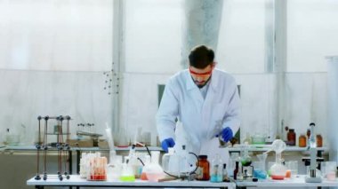 Bilim adamı laboratuarında güvenlik ekipmanlarıyla çalışan bir adam havai fişek yapmaya çalışıyor. Kameranın önüne biraz toz ekliyor.