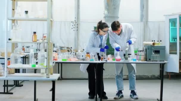 Retro chemisch laboratorium twee wetenschapper vrouwelijk en de mens maken chemische vloeistof experiment in de glazen buis ze geconcentreerd werken — Stockvideo