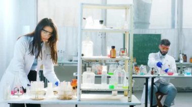 Kimya laboratuarında iki bilim adamı ve kadın cam küvet kullanarak bir deney üzerinde çalışıyorlar. Test yapmak için kimyasal bir reaksiyon ekliyorlar.