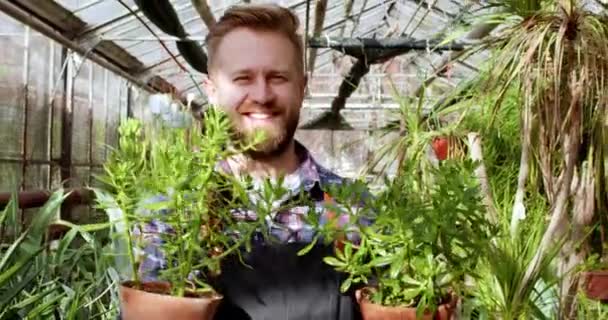 Gros plan sur la caméra souriant grand homme charismatique gros plan tenant deux pots de fleurs et regardant droit vers la caméra — Video