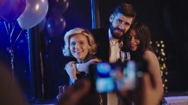 Öğrenci partisindeki karizmatik bayanlar ve akıllı telefon için poz veren bir adam hatıralar için fotoğraf çekiyorlar. Gülümsüyorlar ve rahatlıyorlar.