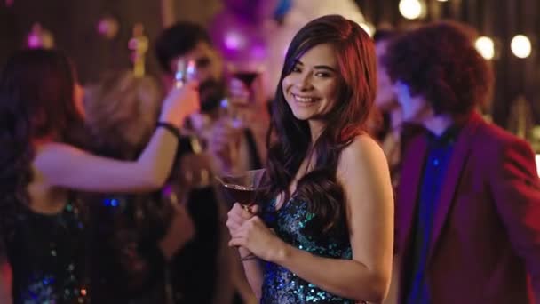 Idealnie wyglądająca pani w błyszczącej sukience patrząca prosto w kamerę i ciesząca się imprezową nocą pijąc koktajl — Wideo stockowe