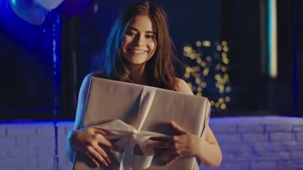 Doğum günü partisinde mutlu bir şekilde gülümseyen güzel bir bayan elinde büyük bir hediye kutusuyla kameraya bakıyor ve poz veriyor. — Stok video