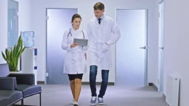 Başhekim ve meslektaşı doktor bayan hastanın teşhisini görmek için dijital tablet kullanarak hastane koridorunda yürüyorlar.