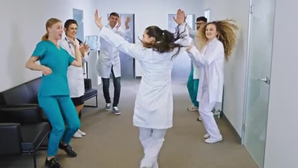 Lächelnd große aufgeregte Ärzte und Krankenschwestern in einem modernen Krankenhausflur tanzen und genießen die gemeinsame Zeit — Stockvideo