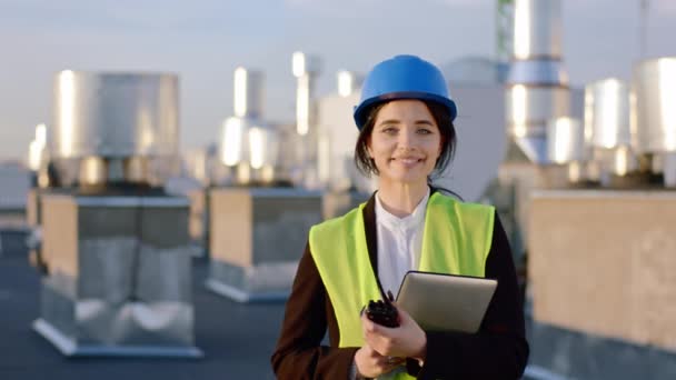 Primo piano per la fotocamera bella signora ingegnere sorridente grande mentre tiene tablet digitale e razionamento indossa casco di sicurezza — Video Stock