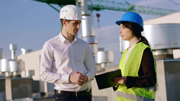 Beautiful architect woman explain some plans of construction to the main engineer they discussing together wearing safety helmets — Stock Video