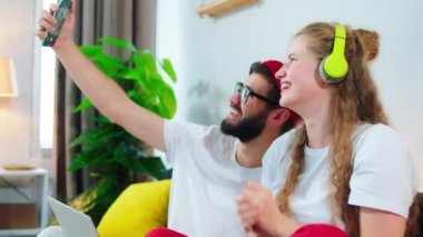 Büyük gülüşlü güzel bir bayan ve güzel bir adam evdeki kanepede oturmuş kulaklıklardan müzik dinlerken telefondan birkaç fotoğraf çekiyorlar. ARRI 'de çekilen