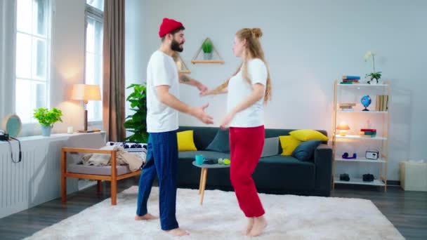 En pijama en casa sonriendo gran pareja carismática en casa en la moderna sala de estar bailando romántico juntos disfrutando del momento — Vídeos de Stock