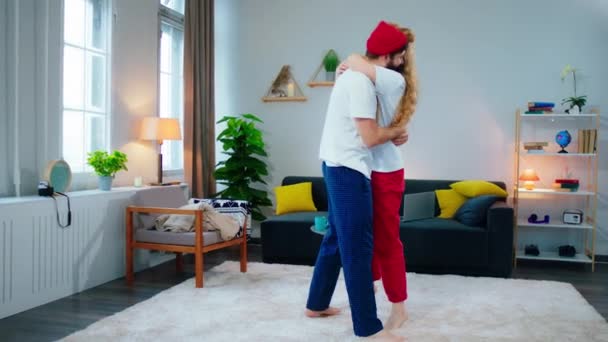 En pijama en casa en la sala de estar abrazando y bailando pareja joven romántica que disfrutan del momento juntos tienen una cara sonriente — Vídeo de stock