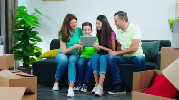 在沙发上，有魅力的大孩子和他们的父母搬到一所新房子里，他们用数字平板电脑分析房子的未来设计 — 图库视频影像