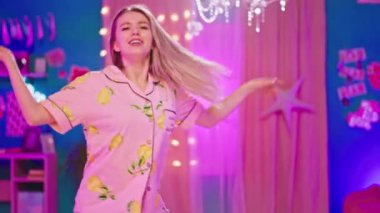 Büyük bir yatak odasında güzel sarışın kadın kameranın önünde dans ediyor ve sabahları pijamayla heyecanlanıyor.