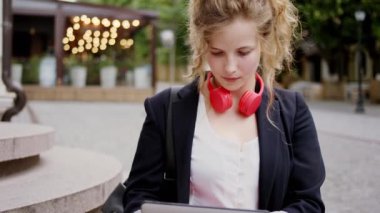 Sokağın ortasında dijital elektronik tablet kullanan çekici genç bir kadın konsantre olmuş ve gülümseyen sevimli bir yazı yazıyor.