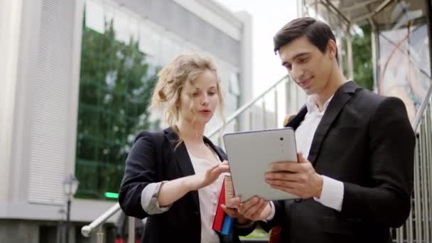 Charismatische man zakenman en zijn assistent vrouw blond haar met behulp van elektronische tablet om iets te analyseren in de voorkant van het bedrijfsgebouw — Stockvideo