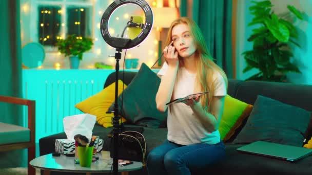 Em casa no sofá bonita olhando senhora beleza blogger usando um smartphone e anel de luz para capturar um vídeo de uma maquiagem para sua conta de mídia social. Tiro em ARRI Alexa — Vídeo de Stock