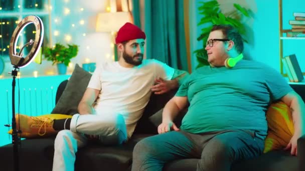 Em casa no sofá dois estudantes caras ter uma conversa amigável um do cara são obesos eles têm um tempo amigável juntos — Vídeo de Stock
