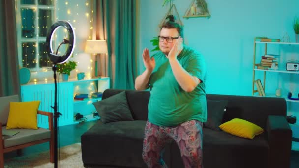 En stor karismatisk kille hemma i vardagsrummet dansar roligt att spela in video för hans sociala medier konto med hjälp av en smartphone för att fånga video — Stockvideo