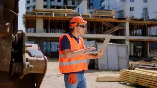 Форман на стройке с помощью ноутбука, чтобы проверить план здания он носит защитные шлемы очки и защитную форму — стоковое видео