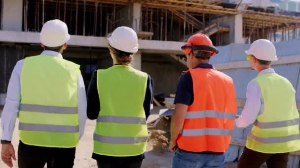 다양 한 젊은 전문가들과 감독들이 방호복을 입고 현장을 걷고 있는 동안 건물 건설을 확인하는 영상을 만들고 있습니다. — 비디오