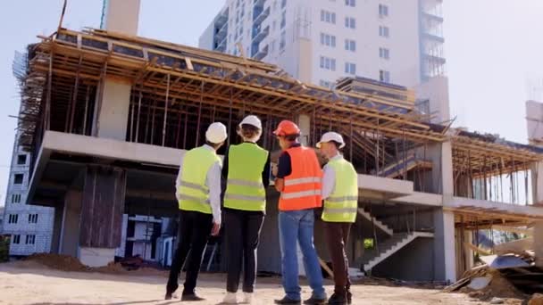 In een grote groep specialisten en voormannen van de bouwplaats hebben zij samen een vergadering om het toekomstige werkplan met beschermende uitrusting te analyseren. — Stockvideo