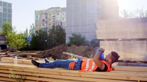 Durmiendo en el trabajo trabajador de la construcción cansado afroamericano se despierta tomar su casco de seguridad e ir a trabajar en un sitio de construcción. 4k — Vídeo de stock