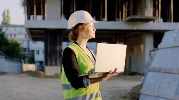 En frente de la mujer ingeniero de cámara con un ordenador portátil que trabaja en el sitio de construcción que llevaba casco de seguridad y equipo de protección — Vídeos de Stock