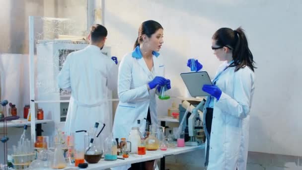 예쁜 여성 과학자와 항 바이러스 백신을 연구하고 있는 그들의 조수는 화학 물질을 섞어 디지털 태블릿에 공식을 작성 했습니다. — 비디오