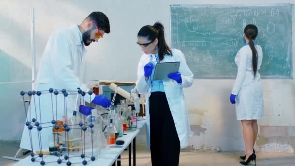 Scientist colleagues together working on a experiment they mixed the chemical substance and write on the digital tablet the results other lady write some formula on the blackboard. Shot on ARRI Alexa — Stock Video