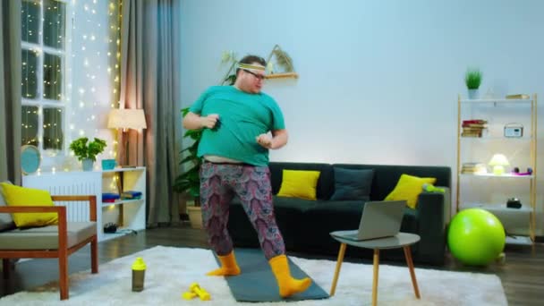 Egy elhízott ember harcművészetet végez a nappaliban egy jóga szőnyegen, egy harcművészeti órán van online. — Stock videók