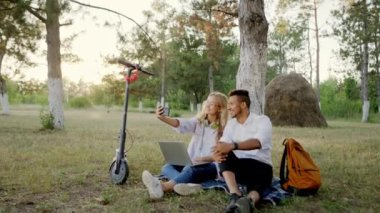 Doğanın ortasında güzel ve karizmatik bir çift akıllı telefonu kullanarak selfie çeker. Elektrikli scooterla piknik yaparlar.