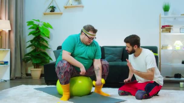 Thuis op de vloer een man samen met zijn zwaarlijvige man doet workout om een gezond lichaam en los gewicht te krijgen — Stockvideo