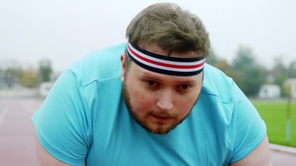 Чарісматичний ожиріння молодий хлопець на стартовій лінії на стадіоні готується бігти крупним планом перед камерою — стокове відео