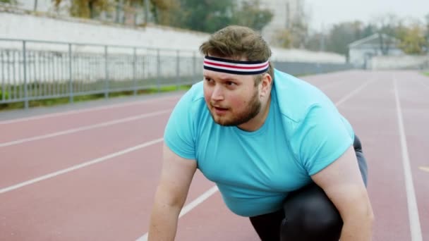 Başlangıç çizgisindeki spor kıyafetli yakışıklı şişman adam dışarıdaki stadyumda sıkı bir antrenmana hazırlanıyor. — Stok video