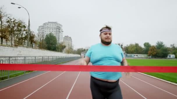 肥満の男のためのマラソンを実行している彼は幸せなスタジアムでフィニッシュラインに到着し、彼は実行するために停止する興奮 — ストック動画