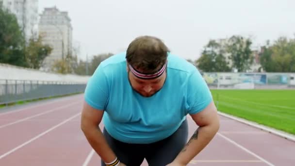 출발선에서 비만 한 젊은 남자는 건강 한 생활을 시작하기 위해 운동복을 입고 경기장에서 달릴 준비를 한다. ARRI 알렉사 미니 촬영 — 비디오