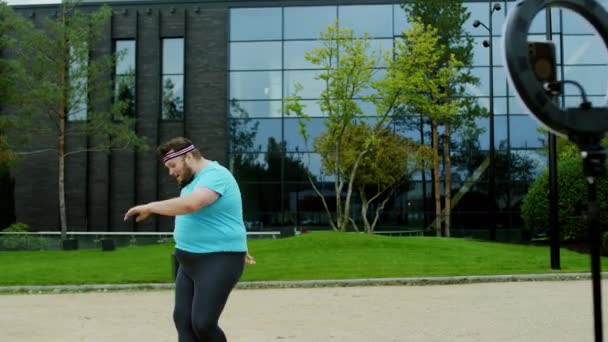Tančící zábavný obézní chlap vedle velké moderní budovy má na sobě jógu oblečení je velmi vzrušený a charismatický. Shot na ARRI Alexa Mini — Stock video