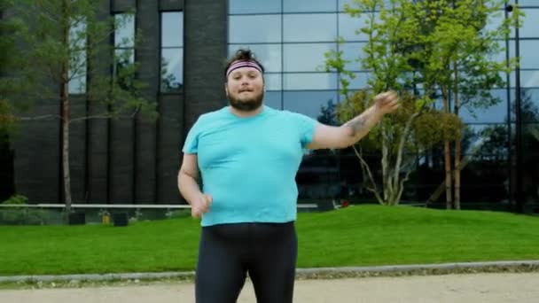 Gut aussehender, fettleibiger Mann außerhalb eines modernen Gebäudes, der sein Workout Aerobic macht er trägt Sportkleidung er ist sehr aufgeregt — Stockvideo