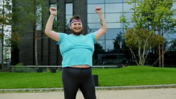 Zdravý životní styl obézní chlap cvičit aerobik venku vedle moderní budovy šťastný a vzrušený, že strečink ruce — Stock video