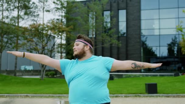 Jóga pózuje jako obézní muž před kamerou, natahuje tělo před moderní budovu. 4k — Stock video