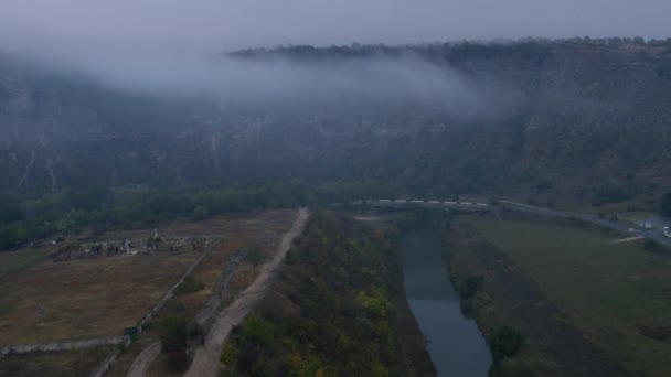 Delante de la cámara tomando video con un dron en un hermoso lugar de la naturaleza con un río y una montaña forestal y rocas con la niebla sobre el paisaje — Vídeos de Stock