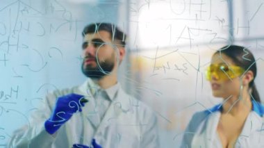 Yakışıklı genç kadın ve erkek bilim adamı çok heyecanlı. İlaç laboratuarındaki saydam tahtaya kimyasal formülü yazın.