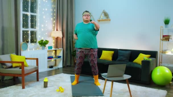 Il y a un gros gros homme sur le tapis portant une chemise verte et un pantalon hippie, il frappe l'air, il est dans une pièce lumineuse et les plans de la caméra se rapprochent de lui et repartent. — Video