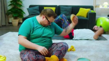 Koca şişman adam yemek için bir hamburger aldı sonra fikrini değiştirdi ve arka planda egzersiz yapmaya başladı. Diğer adam altılı bira almak için mekik çekiyordu.