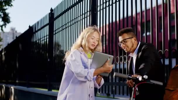 Après le cours universitaire, deux étudiants afro-américains et une jeune femme aux cheveux blonds discutent ensemble d'une dame tenant une tablette numérique pour montrer quelque chose à son collègue — Video