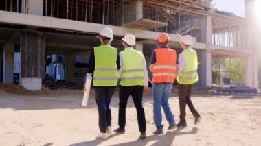 İnşaatın ortasında çeşitli uzmanlardan oluşan bir grubun videosunu çekiyorlar. İnşaatın planını birlikte analiz ediyorlar.