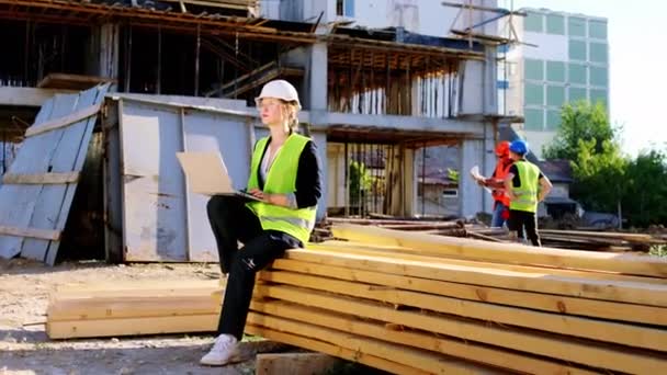 Mladý inženýr blond vlasy dáma s bílou bezpečnostní přilbou pomocí notebooku na staveništi zkontrolovat plán budoucí stavby — Stock video