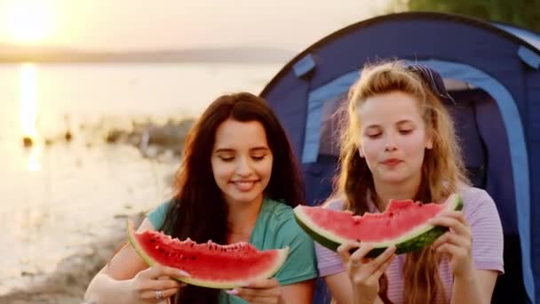 Acercamiento a la cámara dos señoras carismáticas tienen un tiempo de picnic junto al lago que comen una sabrosa sandía y sonriendo a lo grande — Vídeo de stock