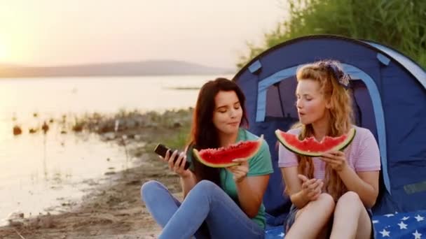 Csodálatos naplemente mellett egy nagy tó két gyönyörű hölgy egy nagy mosollyal érezze jól magát eszik egy kis görögdinnye és érzés nyugodt és boldog — Stock videók