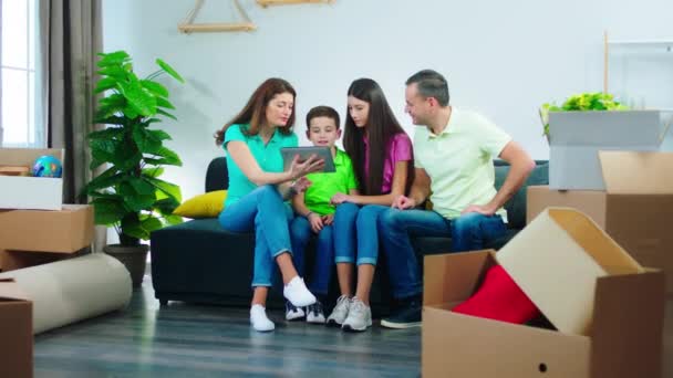 У великій вітальні зрілі харизматичні батьки та їхні діти насолоджуються моментом у новому будинку вони використовують цифровий планшет, щоб побачити майбутній дизайн вітальні — стокове відео