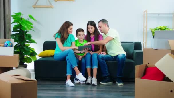 Goed uitziende ouders en hun kinderen genieten van het moment in de moderne woonkamer op de bank ze kijken een film op de digitale tablet na afloop om de dozen uit te laden in een nieuw huis — Stockvideo